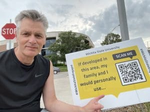 WSU president Dr. Rick Muma poses with a sign that reads "If developed in this area, my family and i would personally use ... " There's also a QR Code and the words "Scan Me."