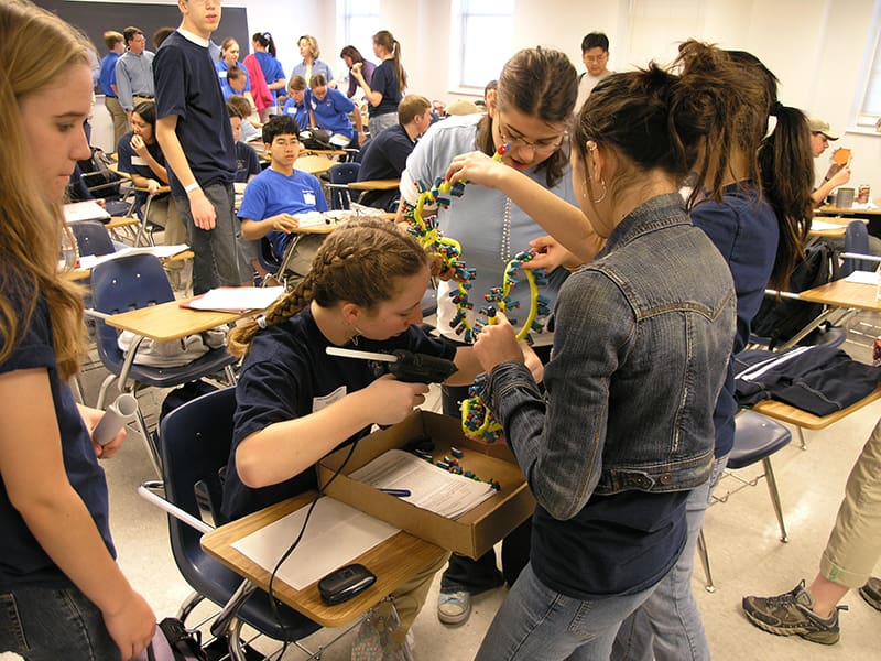 Three students work on a DNA model in a classroom.