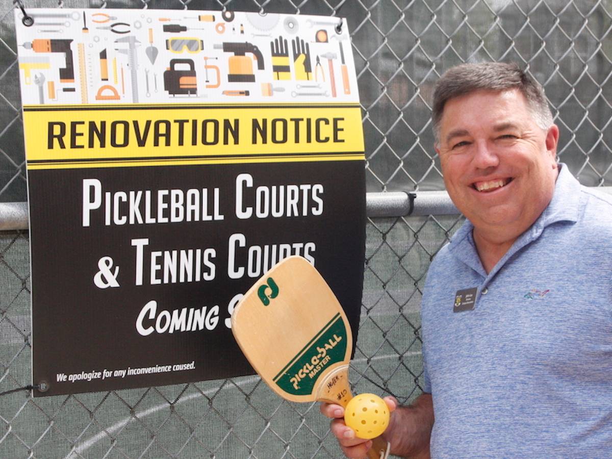 Picture of John Lee, director of Campus Recreation, holding pickleballs in front of sign that reads 'Renovation Notice-Pickleball Courts and Tennis Courts Coming Soon-We apologize for any inconvenience caused.'