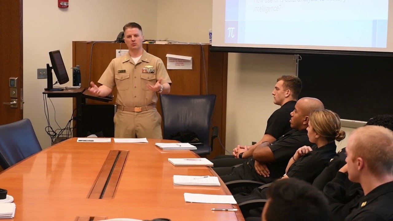 LCDR Joseph M. Hatfield speaks to a roomful of people