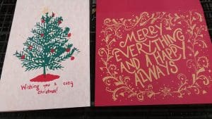 A photograph of two greeting cards, one saying, "Wishing you a cozy Christmas!" the other reads, "MERRY EVERYTHING AND ALWAYS"