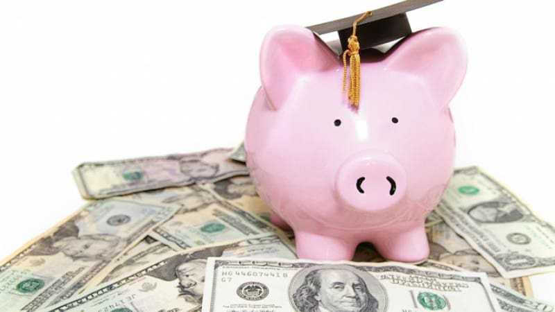 Piggy bank with graduation cap on a pile of money.