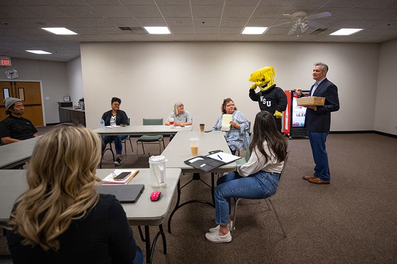 Picture of the staff of Wichita State's Conferences and Non-Credit Services receiving a visit and cookies as part of the Rick Rewards Presentation on Thursday, April 21.