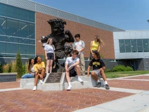 Picture in front of WSU's WMCA featuring seven students posing around the Wu Bronze Statue.
