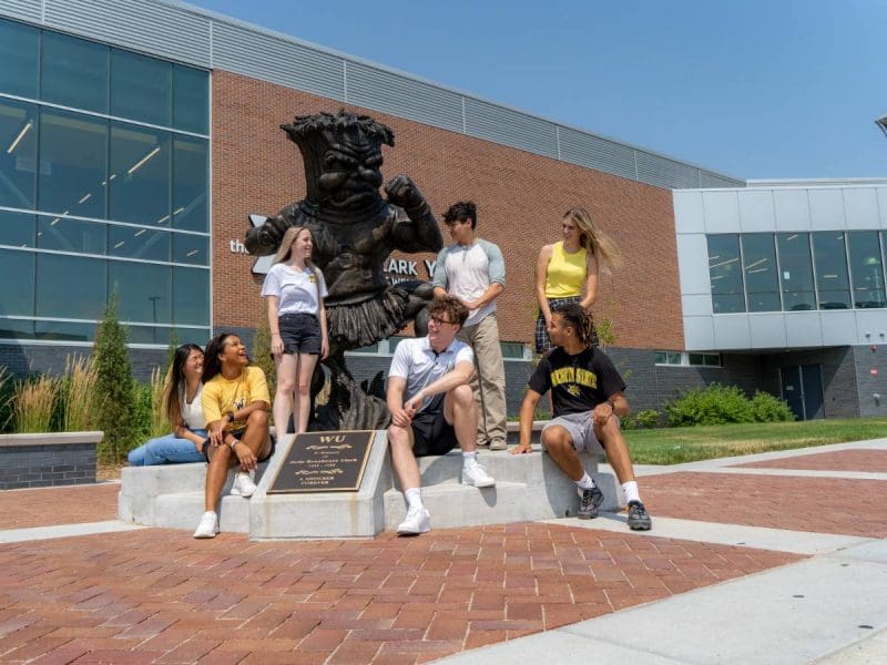 Picture in front of WSU's WMCA featuring seven students posing around the Wu Bronze Statue.