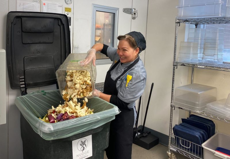 Picture of Khristin Nguyen, a member of the Chartwells kitchen crew, dumps food waste into a composting bin in Shocker Hall