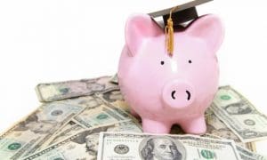 Picture of piggy bank with graduation cap on top of a pile of money.