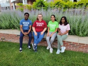 Image of four students outside Rhatigan Student Center wearing WSU blue, red, green and yellow T-shirts.