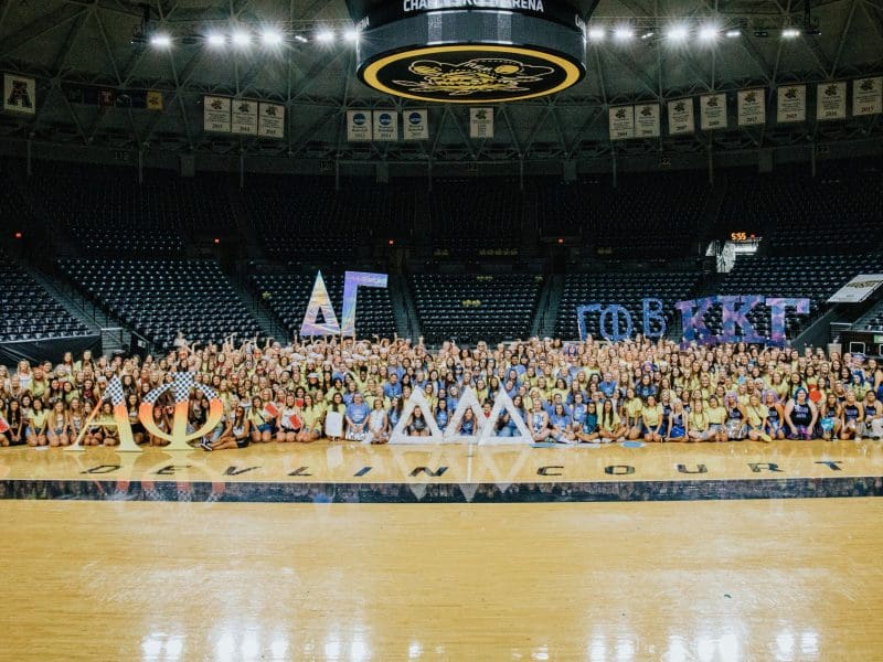 A large group photo of all 5 chapters celebrating on Bid Day. Each chapter is holding up signs in the shape of their chapters' Greek letters.