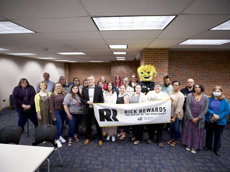 Image of Wu and President Rick Muma posing with University Libraries staff holding a banner.