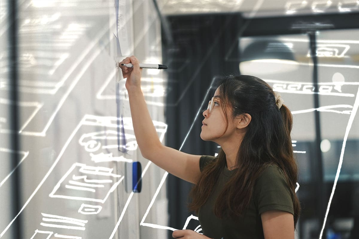 A photo of a person writing on a glass panel.