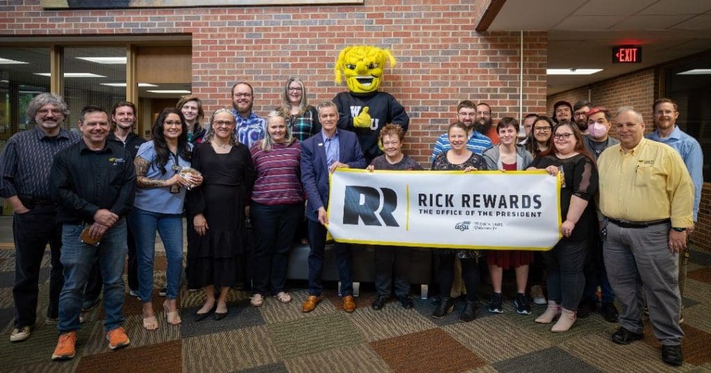 Photo of President Rick Muma with members of the Media Resources Center and WuShock holding up a sign that says "Rick Rewards | The Office of the President."