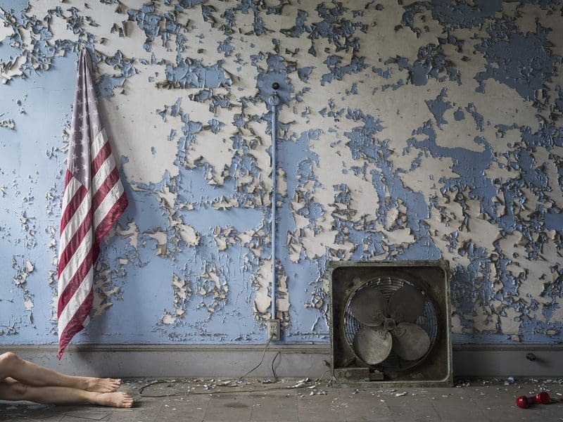 A wall with peeling blue paint, an American flag, a red phone and a women's pair of legs.