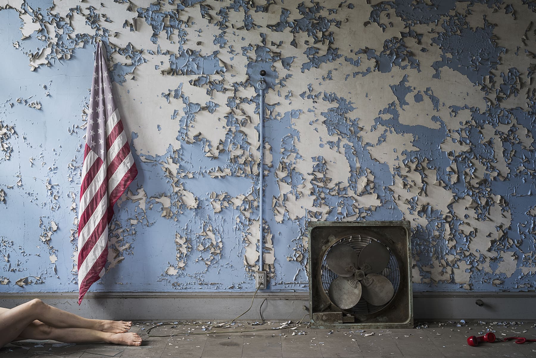 A wall with peeling blue paint, an American flag, a red phone and a women's pair of legs.