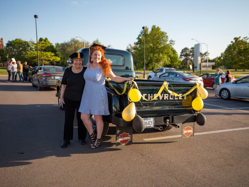 Photo of a previous Commencement Cruise with a student and faculty member posing next to a car decorated for the parade.