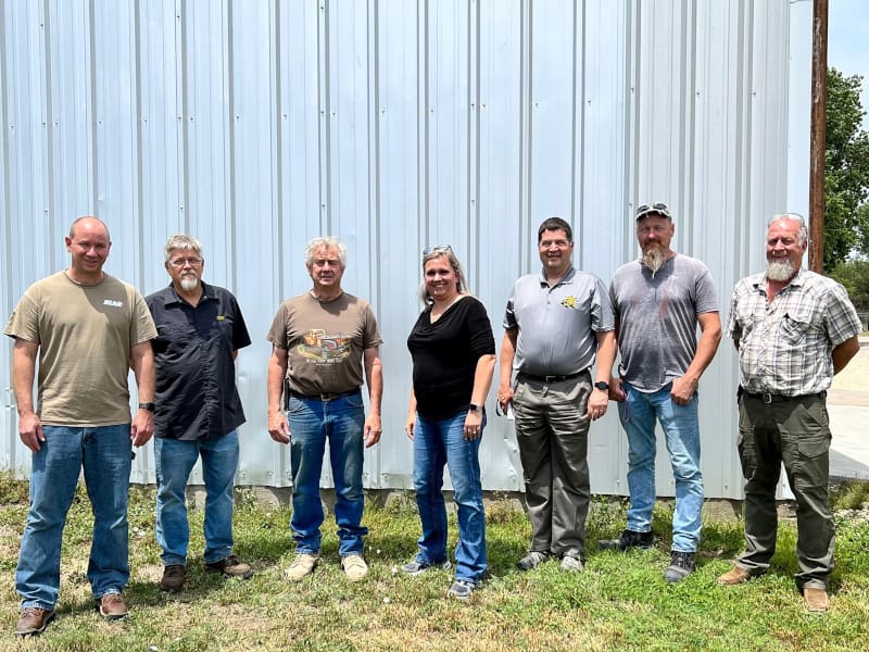 NIAR sustainment team leads and former McFarland employees stand in front of a metal plate.
