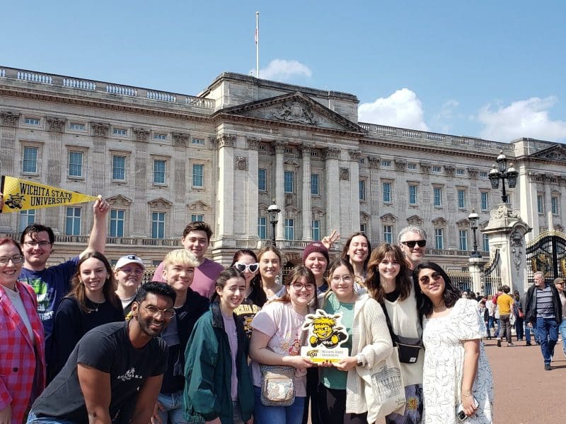 Faculty and students stand in front of Buckingham Palace holding Wichita State and WuShock signs.