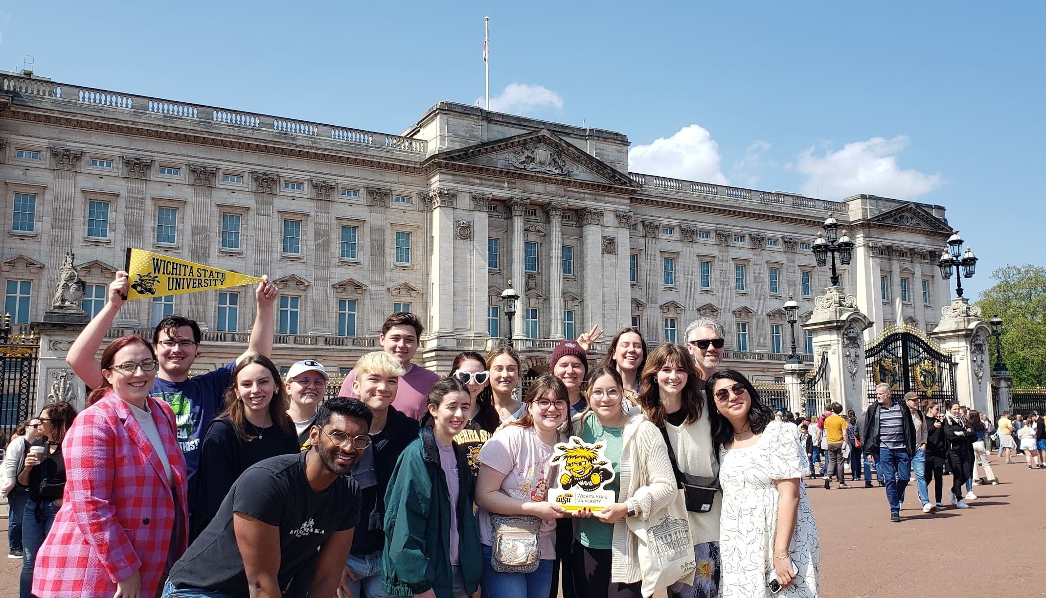 Faculty and students stand in front of Buckingham Palace holding Wichita State and WuShock signs.