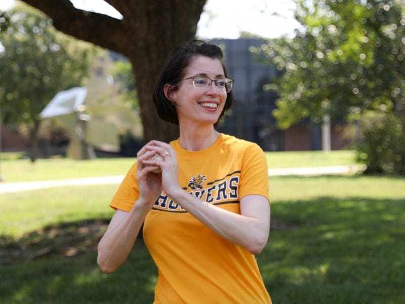 Dr. Jennifer Friend smiling with baseball practicing pitching on campus