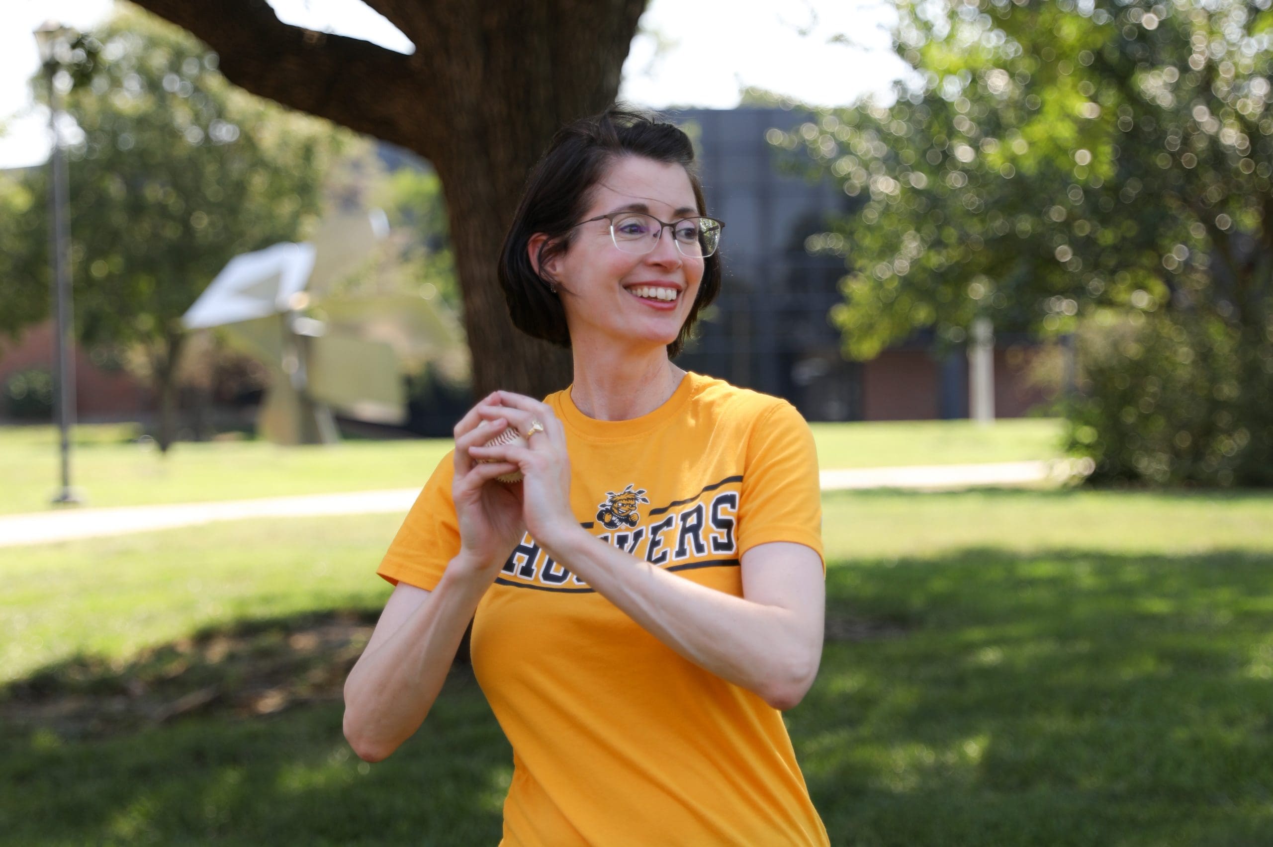 Dr. Jennifer Friend smiling with baseball practicing pitching on campus