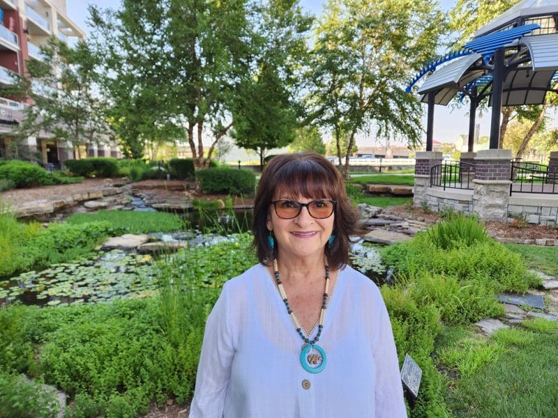 A smiling woman is standing in front of a garden.