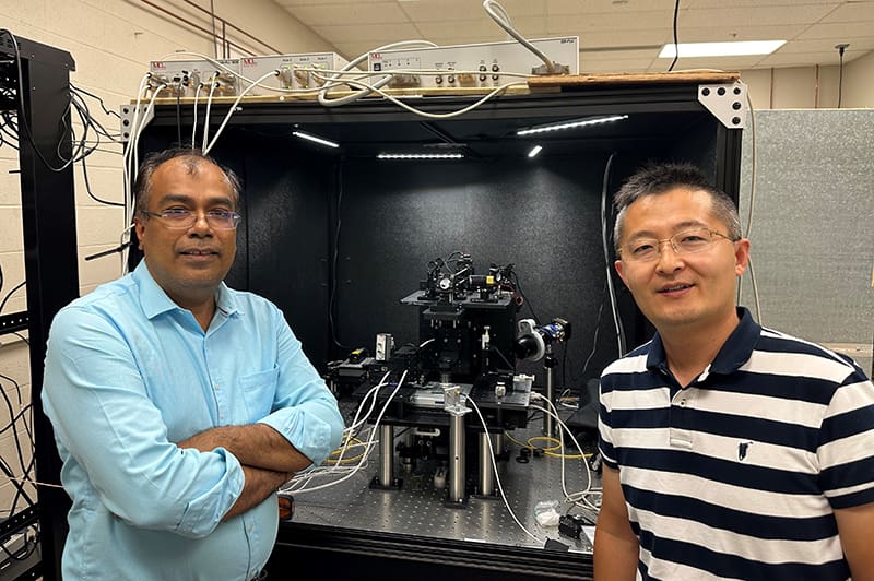 Kapildeb Ambal and Jian Wang stand in front of the single-spin quantum microscope they use to study quantum materials.