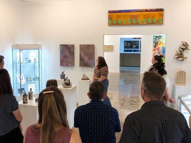 A group of people look at ceramic artwork in a gallery.