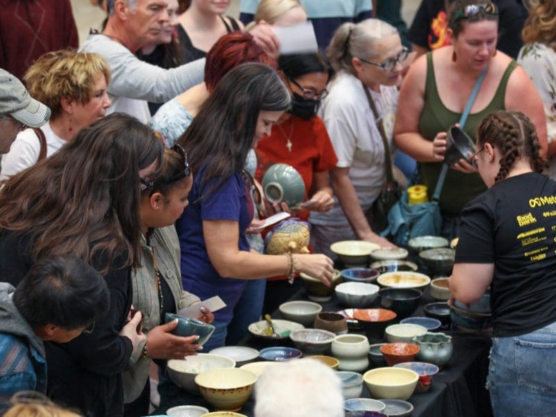 A crowd of people choose a bowl from a large table