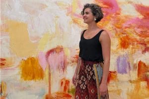 Vivian Zavataro stands in front of a wall splashed with color.