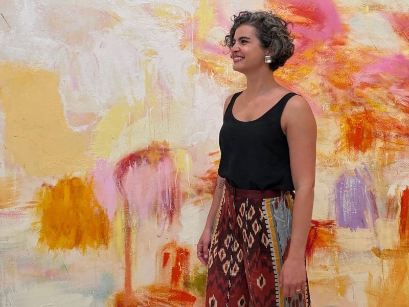 Vivian Zavataro stands in front of a wall splashed with color.