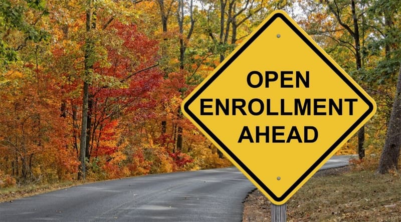 Street sign in a wooded area that says open enrollment ahead