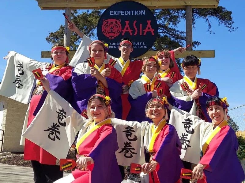 The Tatsumaki Yosakoi team posing in their costumes in front of a sign that reads "Expedition Asia."