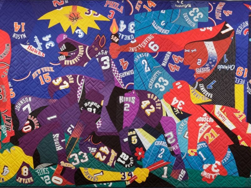 A quilt constructed of sports jerseys by artist Hank Willis Thomas is pictured. This piece is called Guernica.