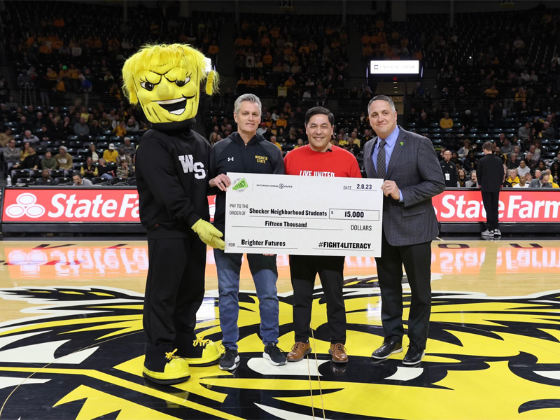President Rick Muma and Kevin Saal hold up a check for $15,000 to the 2023 Fight For Literacy campaign in Charles Koch Arena with WuShock and a representative from United Way