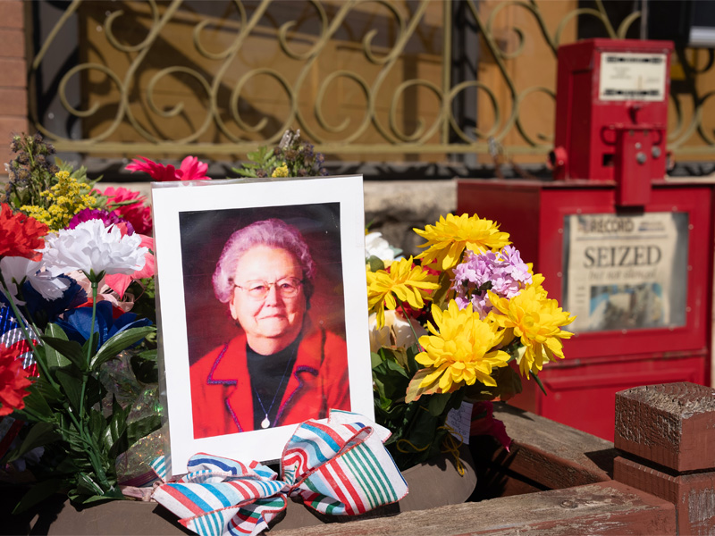 A photo of Joan Meyer sits among flowers with a newspaper station in the background with "SEIZED" as the headline