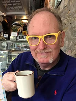 Darren Defrain wearing yellow frame glasses and holding a coffee mug