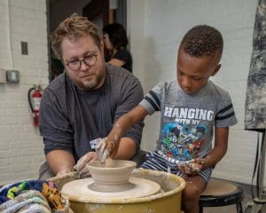 A boy throws a ceramic bowl with the help of a man.