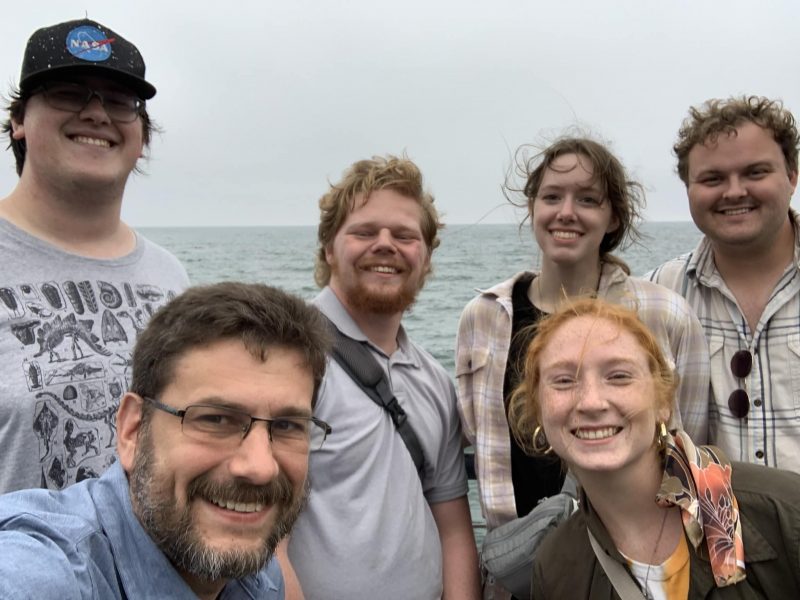 Geology students pose for a photo with the ocean in the background.