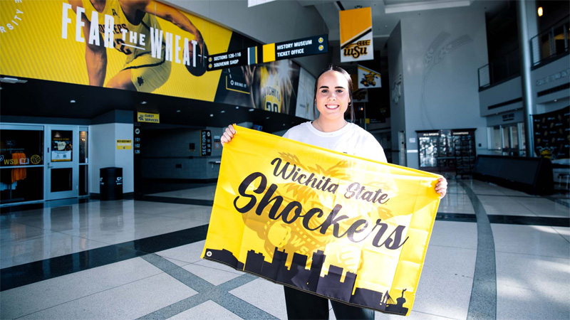 A Wichita State student displays a Wichita State Shocker City Skyline flag in the concourse of Charles Koch Arena