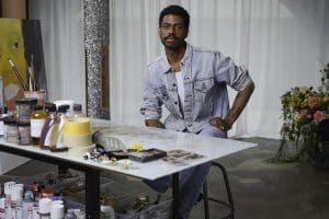 A young black, male-identifying artist is seen at a desk in his studio.