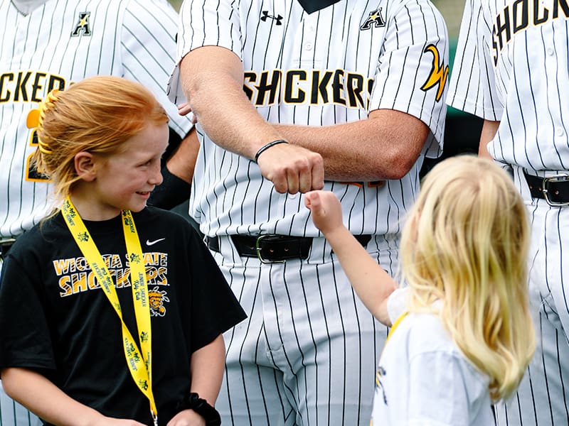 A Jr. Shocker fist bumps a WSU Baseball player on the field before a game