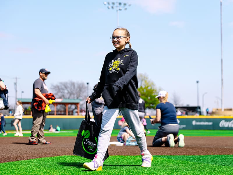A young girl happily collects candy-filled eggs on the field at Eck Stadium