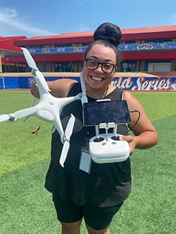 Amaya Harris holds a drone while standing on a baseball field.