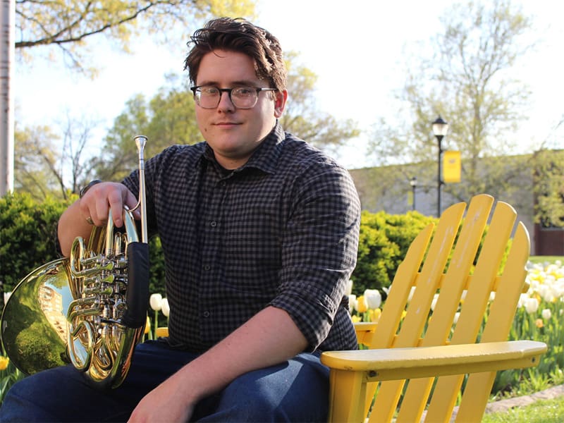 Colby Hutson poses with his French horn for a photo while on campus