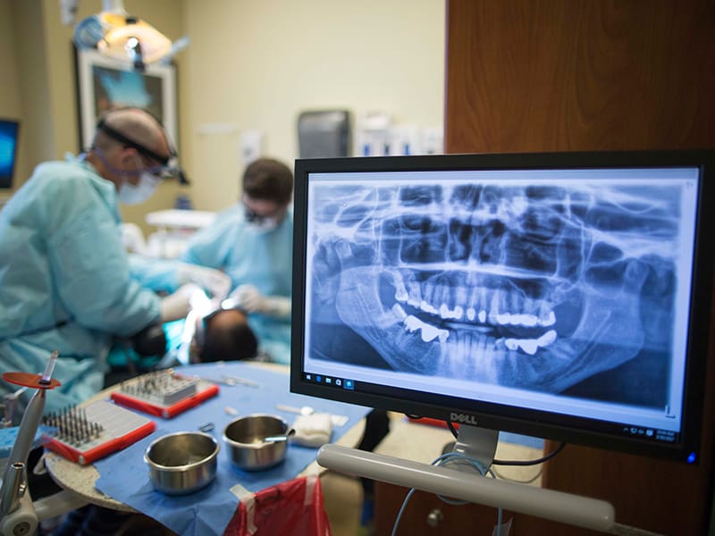 Dental X-ray on a computer screen with dentists working on a patient in the background