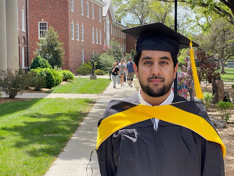 Sayed Mohib Hassan poses outside of Jardine Hall in his graduation regalia