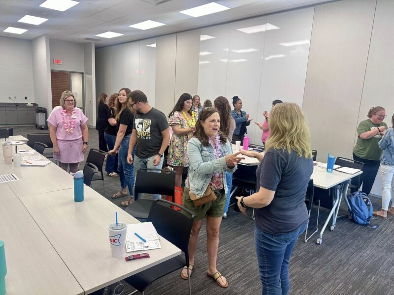 Attendees at the SELebration Conference engage in an interactive activity during a breakout session. Pairs of participants are standing face-to-face, talking and laughing in a bright, modern classroom setting.