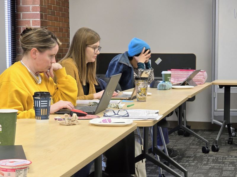 Faculty Erin O'Bryan, Karissa Marble-Flint, and Nadia Kianvashrad sit at a table in front of their laptops working during the Spring Break Faculty Writing Retreat in March 2025.