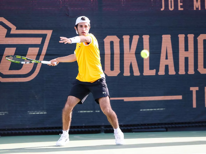 Alejandro Jacome winds up to hit a ball back to the other side of the court. OSU's logo is on the backboard in the background.