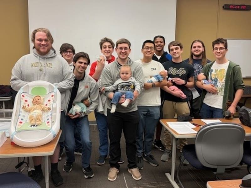 Students in the Sigma Phi Epsilon fraternity pose for a photo during a childcare class given by School of Nursing faculty